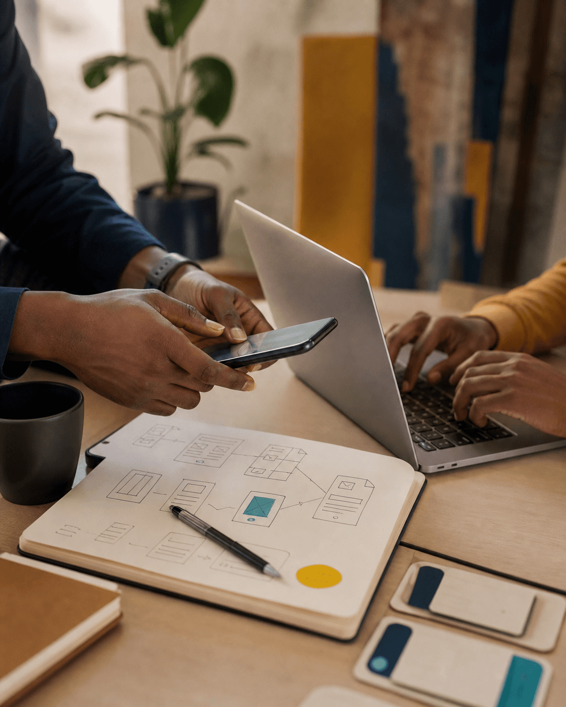 People collaborating around a phone and laptop with product sketches